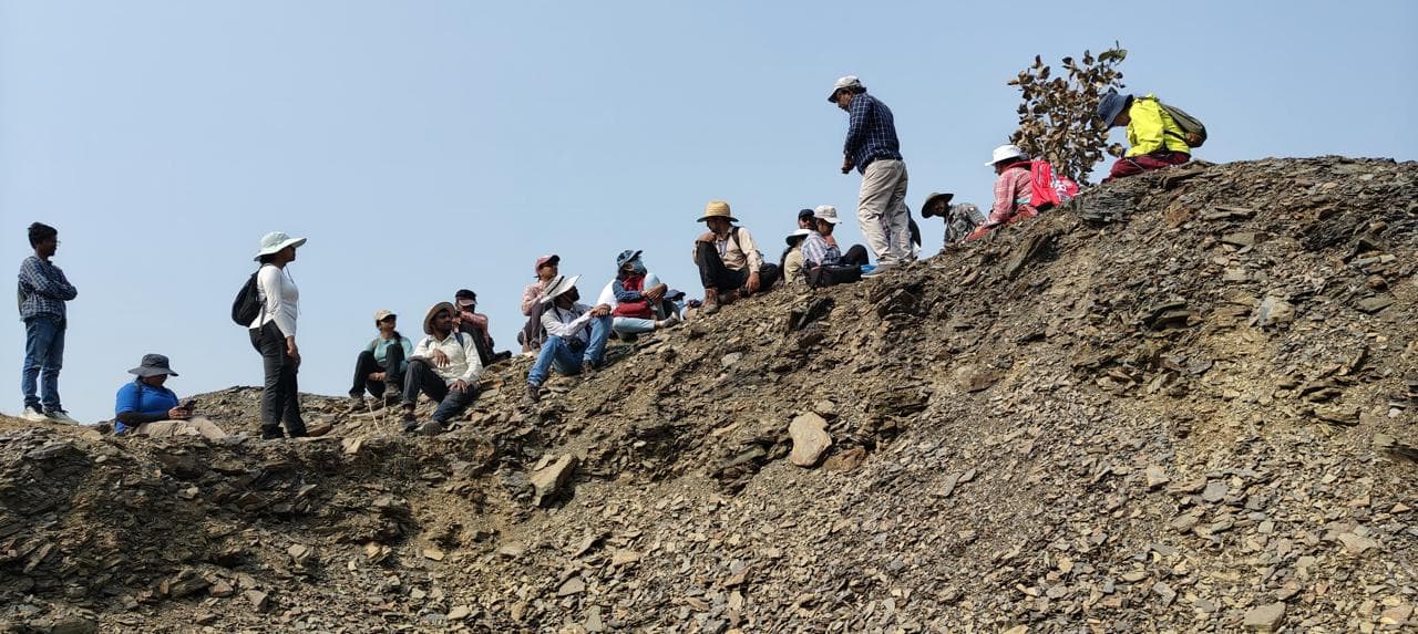 A field team spread along the crest of a steeply dipping shale outcrop
