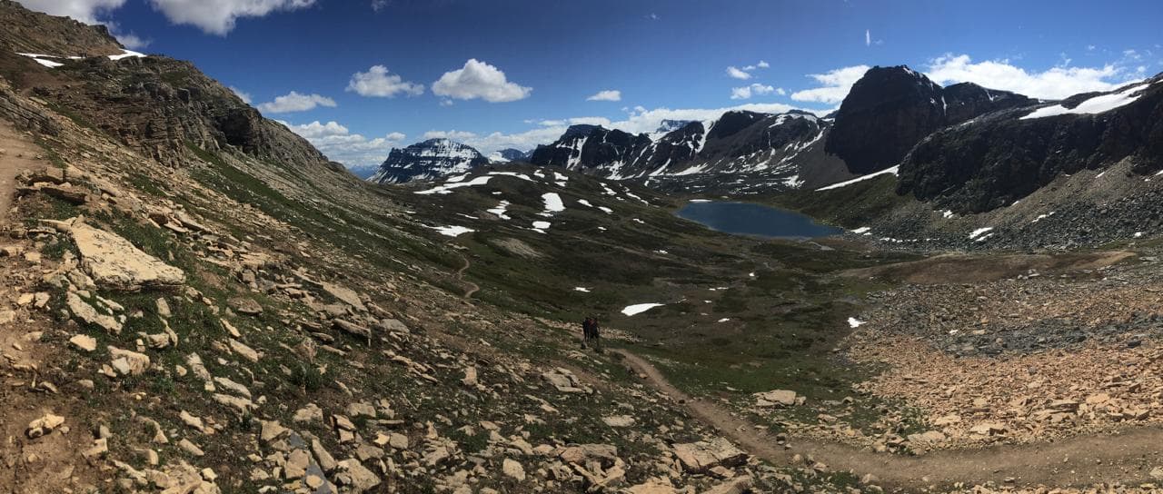 A trail descending toward an alpine cirque lake ringed by snow-streaked peaks
